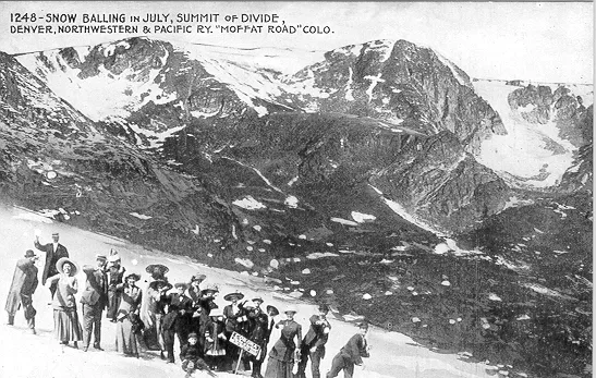 A group of people gathered on a mountainside tossing snowballs. Caption snow balling in July summit of divide Denver