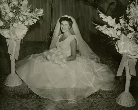 A woman in a bridal dress poses by garlands of flowers