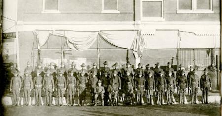 Archival photo of a group of over twenty men in military uniform outside.