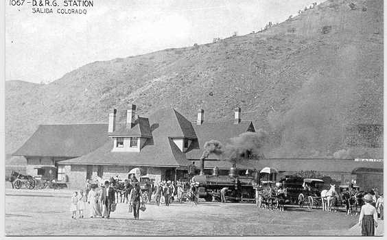 Archival photo of a train station, horse and buggy, and people with suitcases labeled D&RG Station, Salida, Colorado